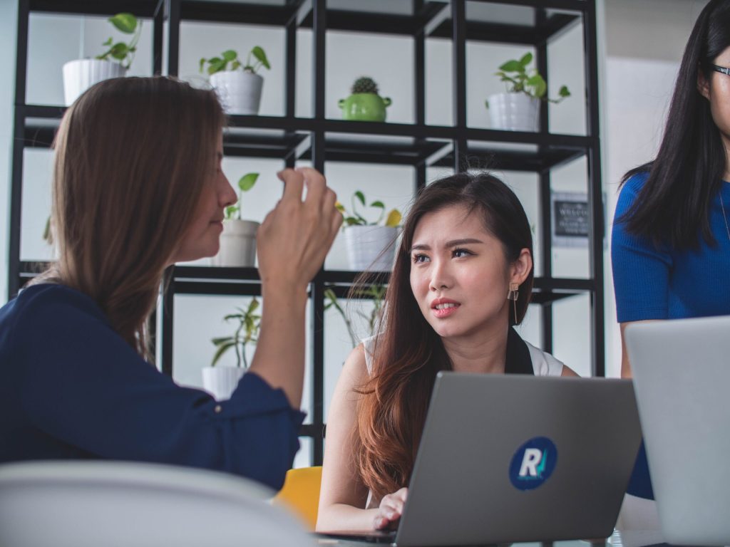 Coworkers talk around laptops at a shared table