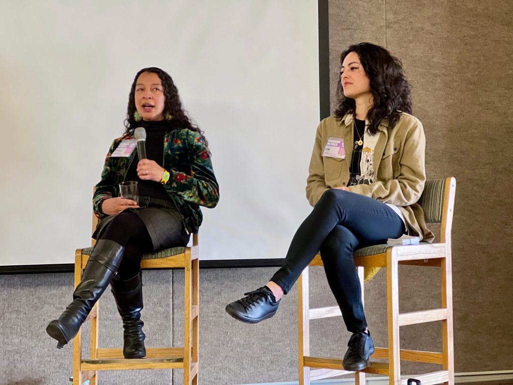 Two women speak from stools on stage during a Founded in FoCo session