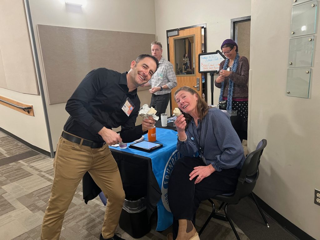 Two attendees smile for the camera at a check-in table at Founded in FoCo 2024